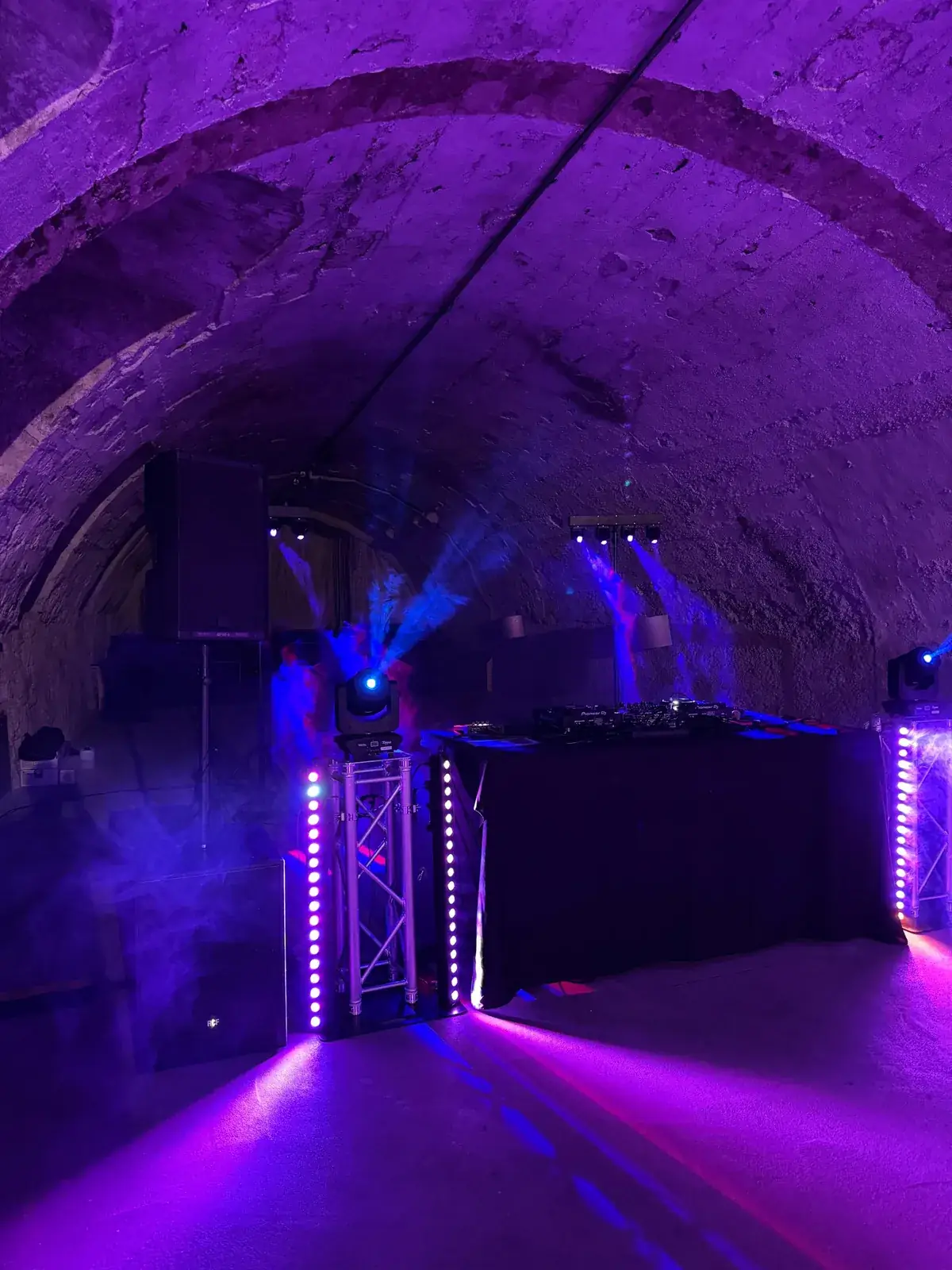 Gewölbekeller von Schloss Tillysburg in violettem Licht mit Moving Heads auf Traversen, LED-Leisten und Lichtstrahlen im Dunst neben dem DJ-Pult