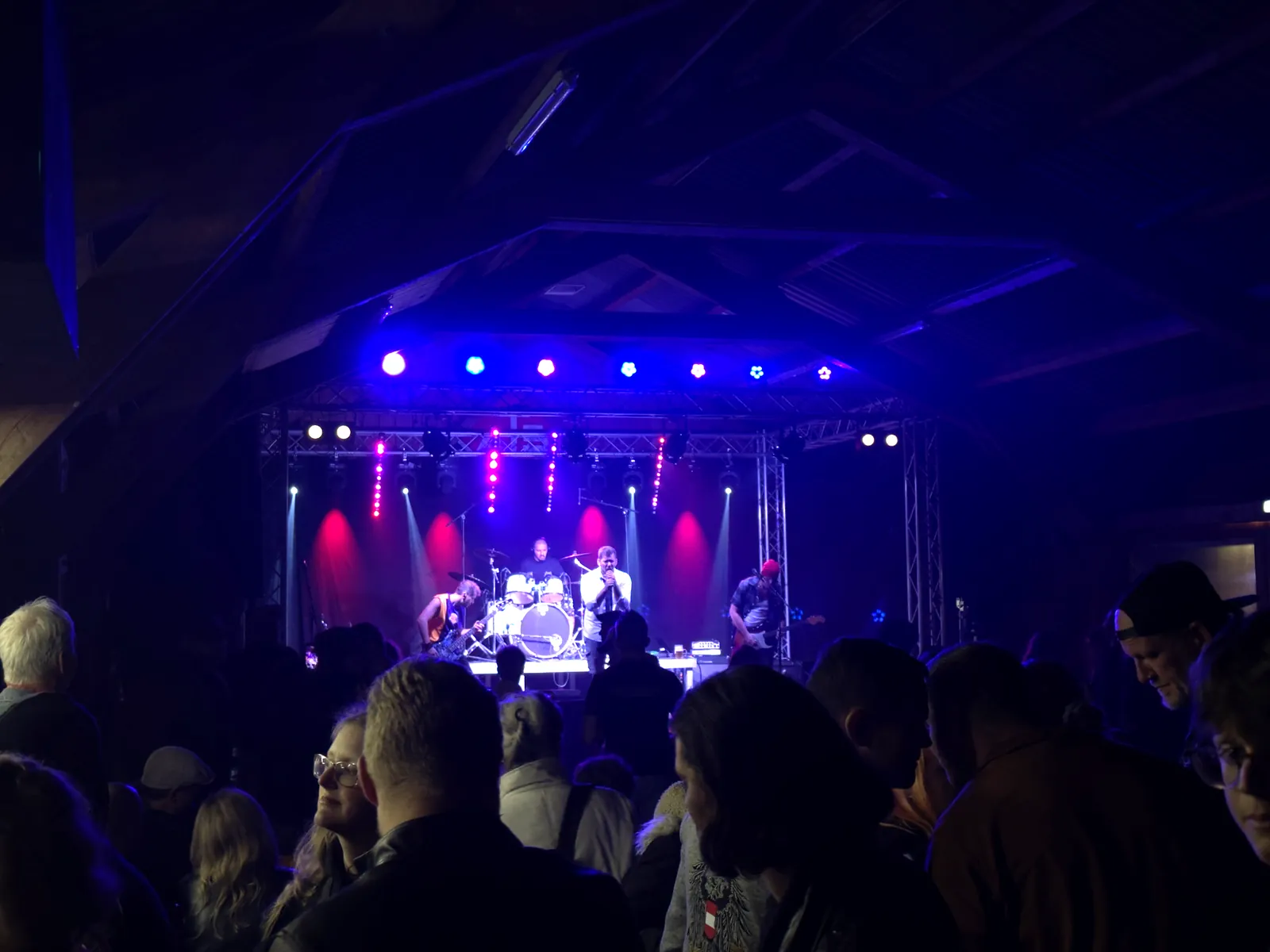 Band beim Hausrock 2026 auf der Bühne unter dem Holzdachstuhl, blaues und rotes Licht, volles Publikum