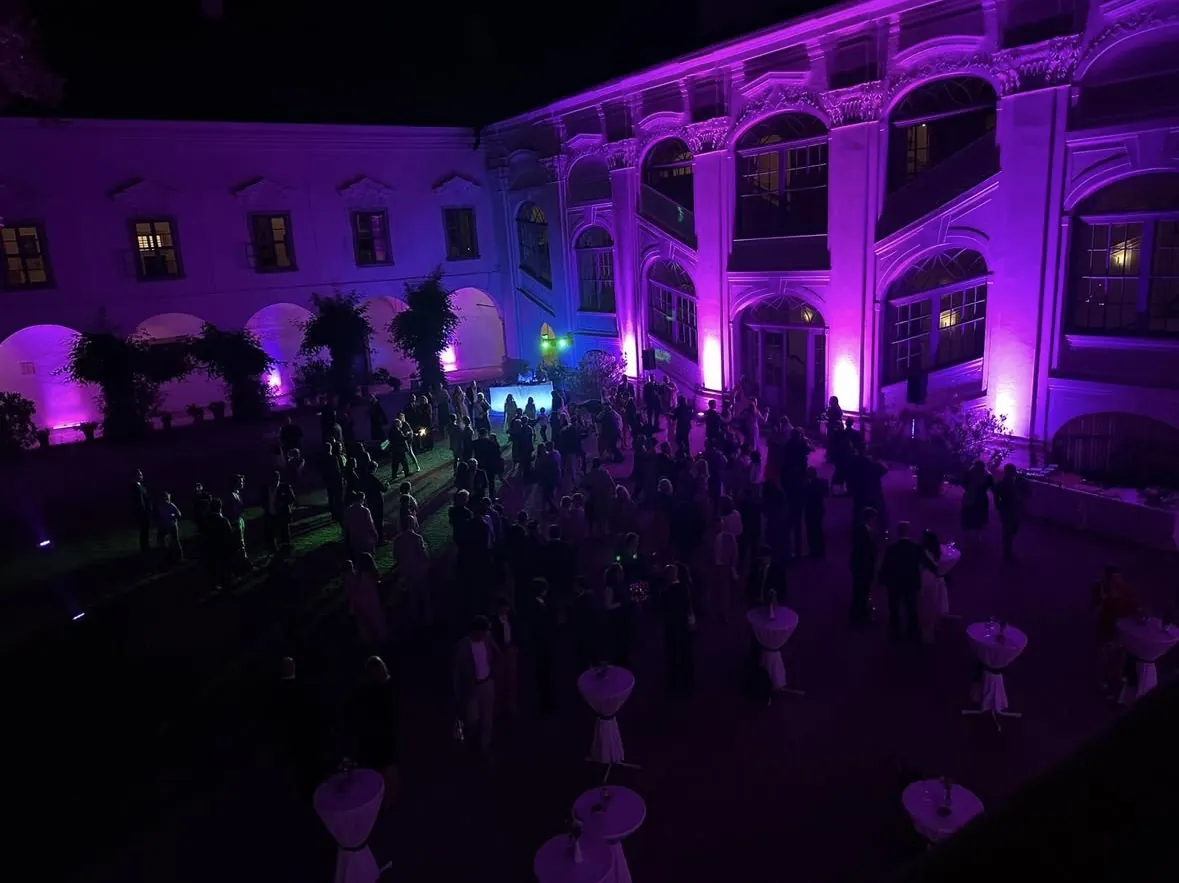 Innenhof von Schloss Tillysburg bei Nacht, Fassade in violettem Licht, Hochzeitsgäste an Stehtischen